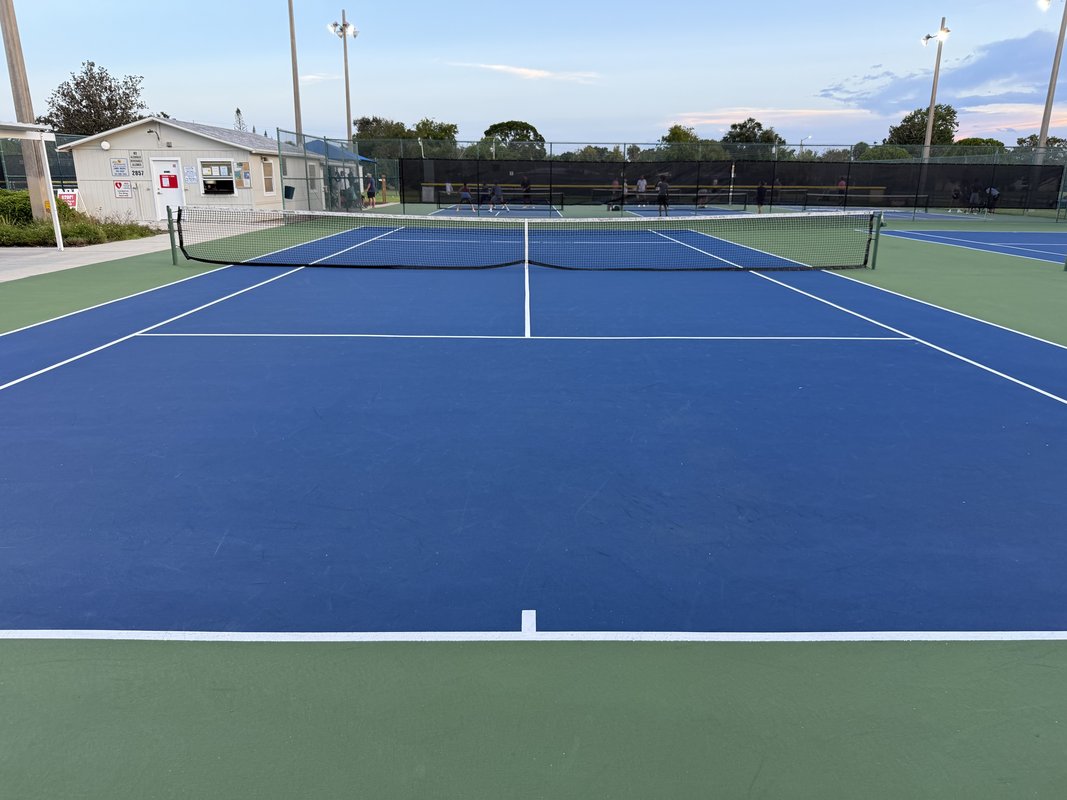 Professionally built tennis court with uniform blue acrylic surface and proper lighting in Florida